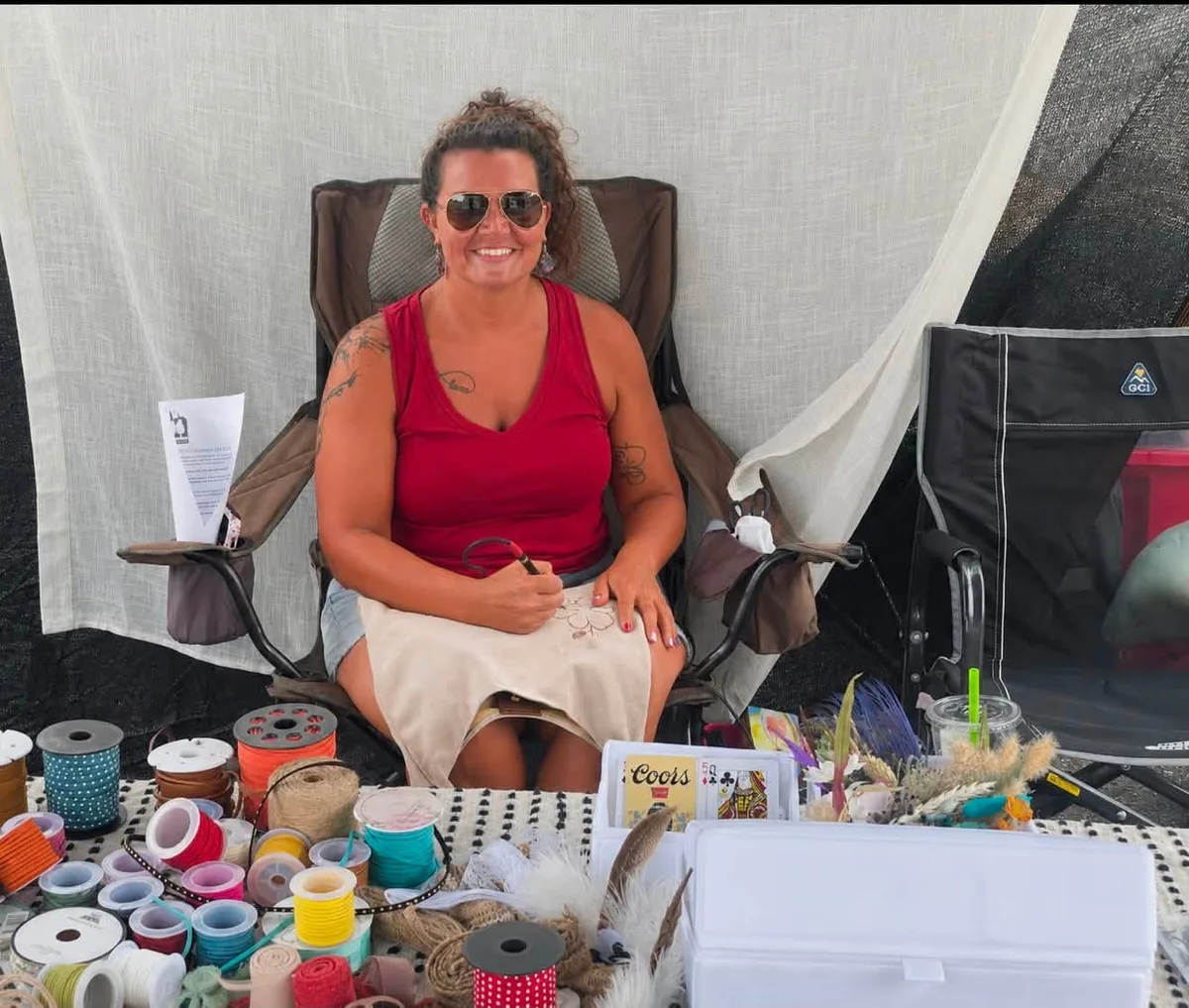 Heather Houser hand-burning a design at her market booth, surrounded by spools of ribbon and dried flowers.