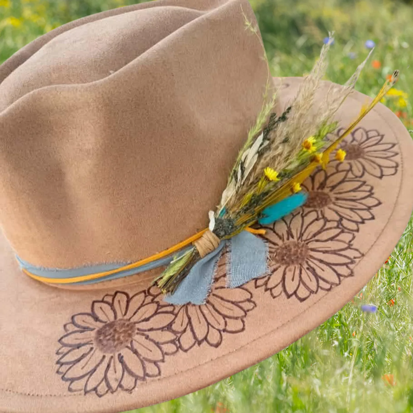 Tan felt hat with a hand-burned floral design, resting in a wildflower field